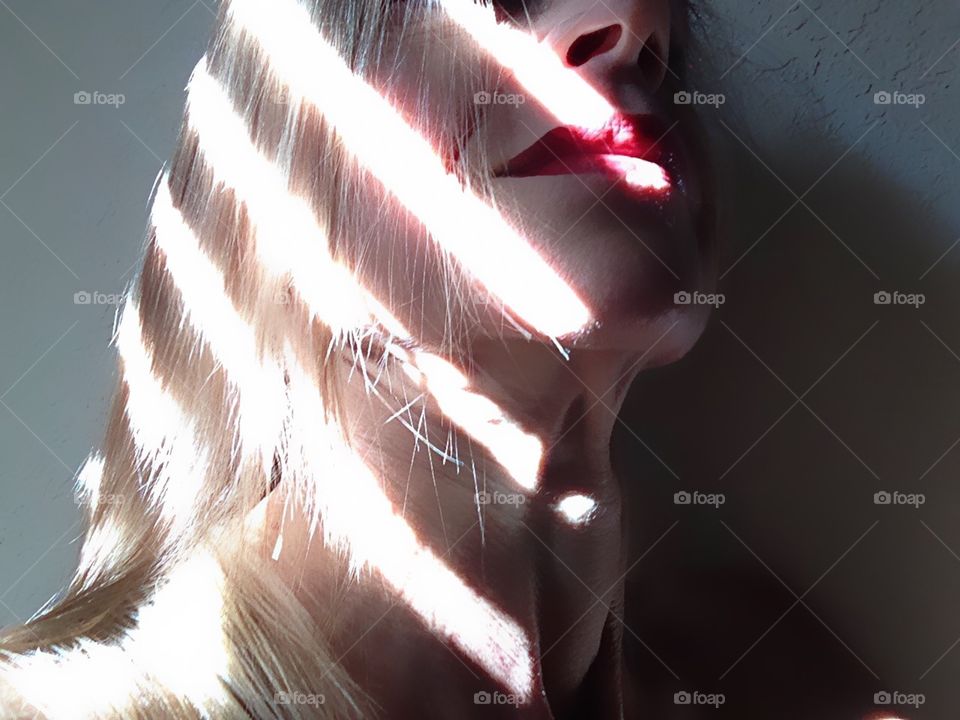 Bright rays of sunlight shine in an interesting pattern on a woman’s face.