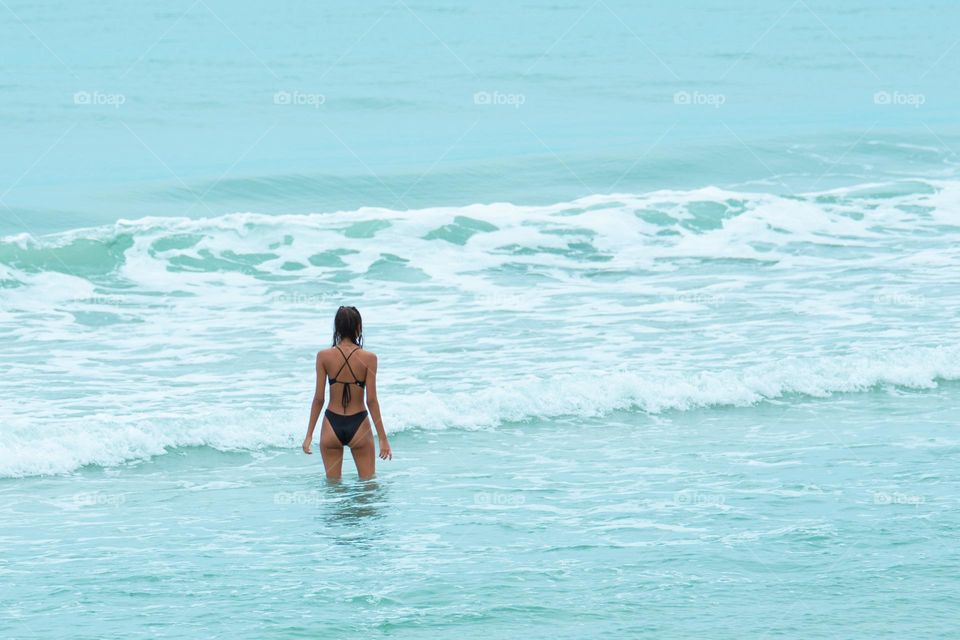 a woman in a black bikini is walking into the beautiful blue ocean waves