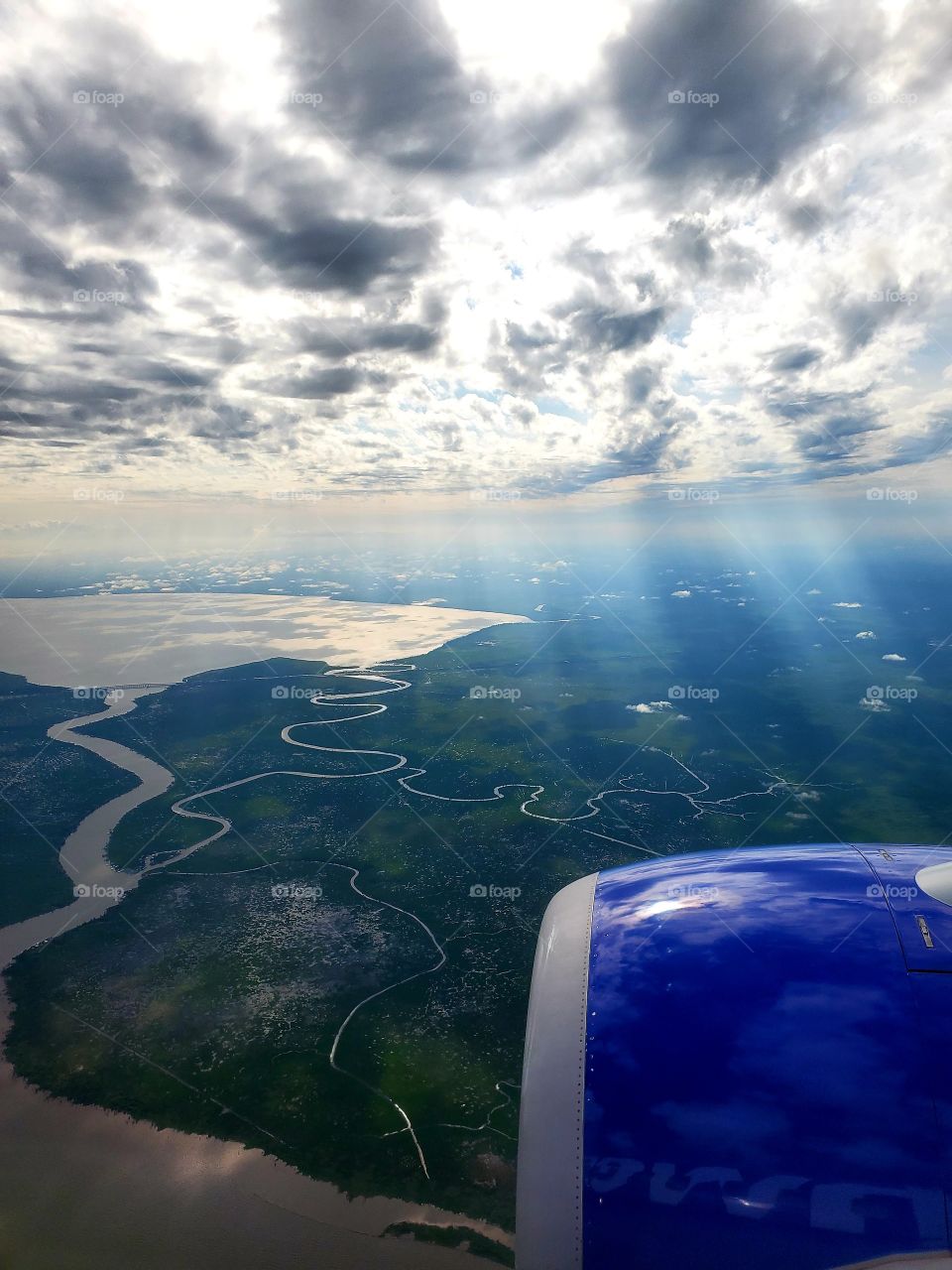 Sunlight shafts shine through broken clouds while flying into New Orleans