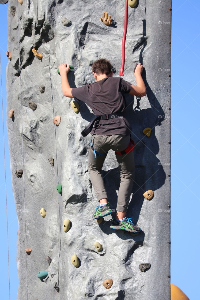 Back view boy rock climbing outdoors 