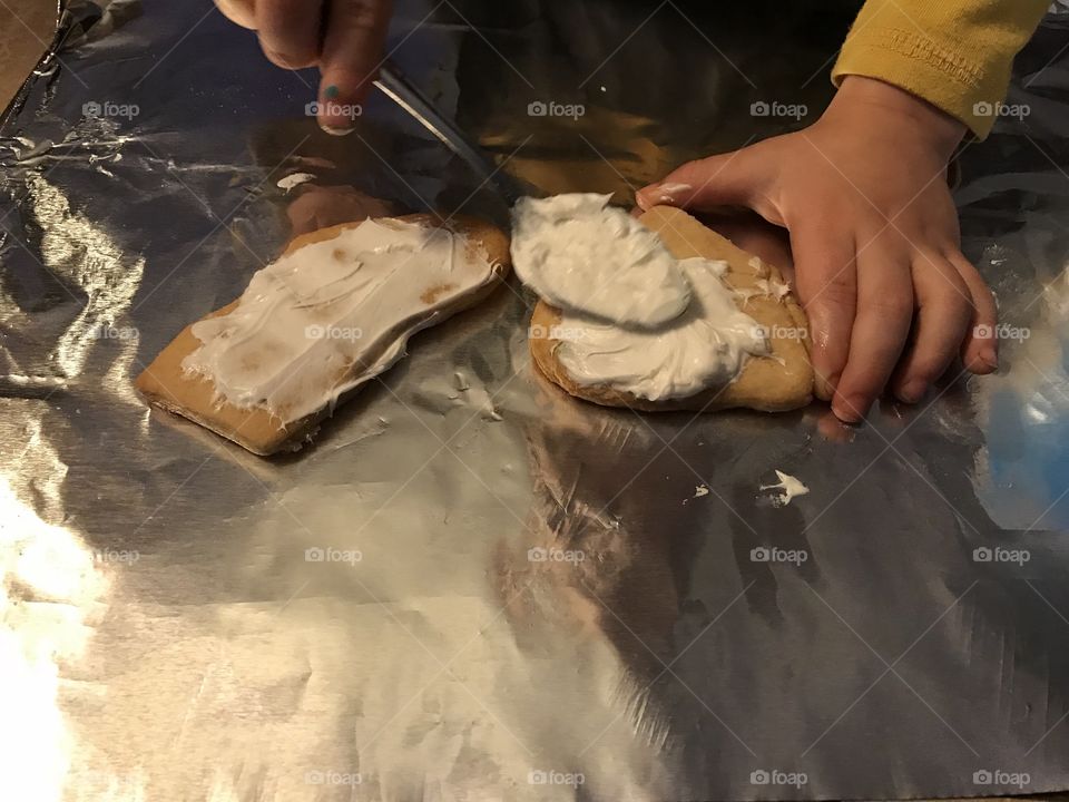 Kid putting icing on sugar cookies with a spoon