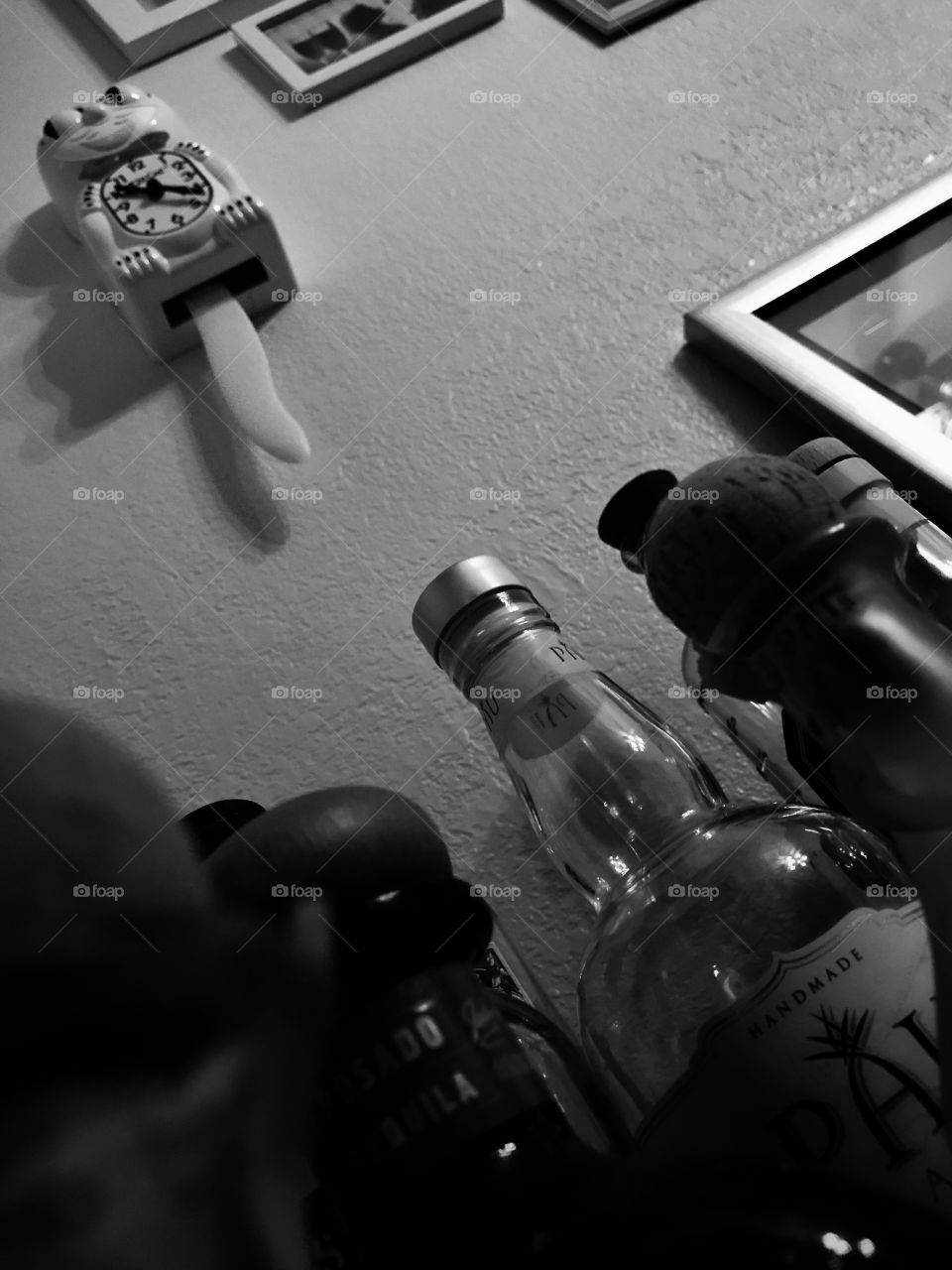 A dark monochrome photo of alcohol bottles looking upward at a kit kat clock. It’s darkly humorous, perhaps even ominous as the clock might indicate timing and something imminent about to happen. Subtle mortality.
