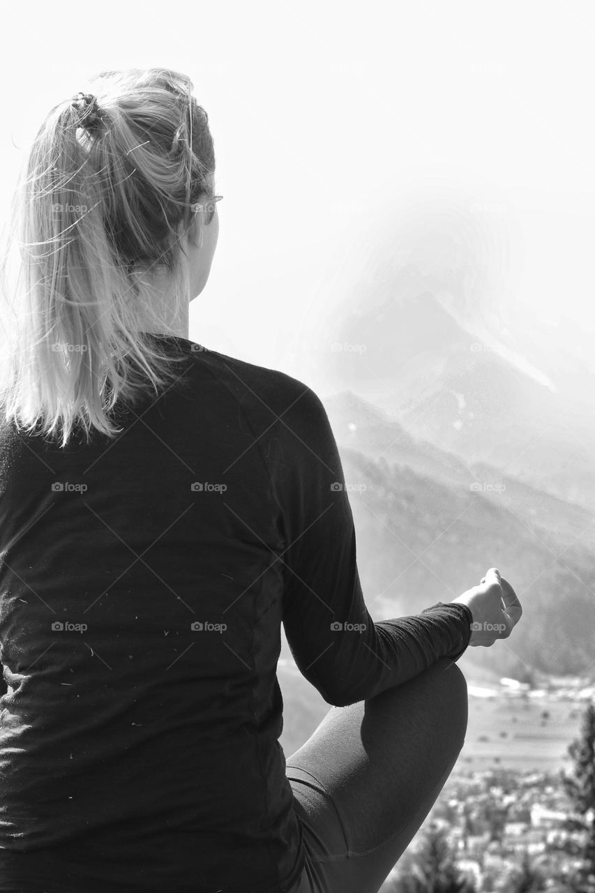 Black and white photo of a meditating woman with a mountain view in foggy weather