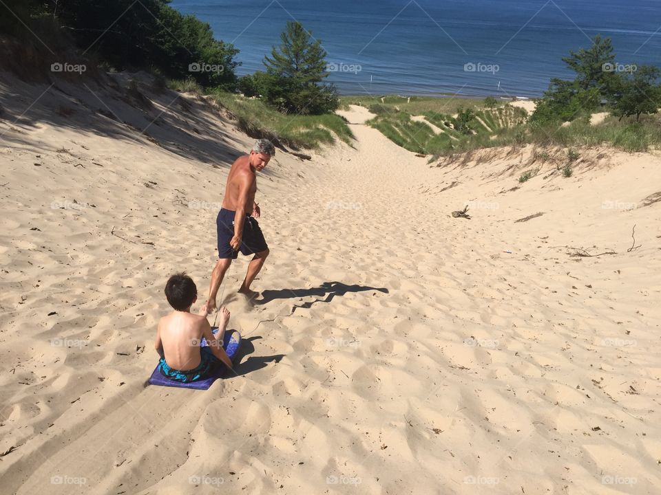 Sand dune fun . Grandpa pulling his grand son on a boogie board down sand dunes 