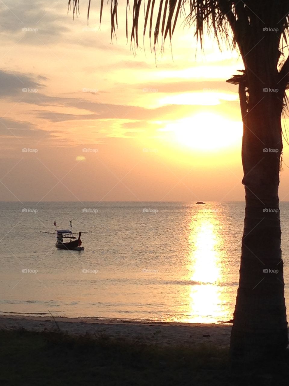 Sun setting over the calm tropical sea. A Thai fishermen sailing his boat to the coast.