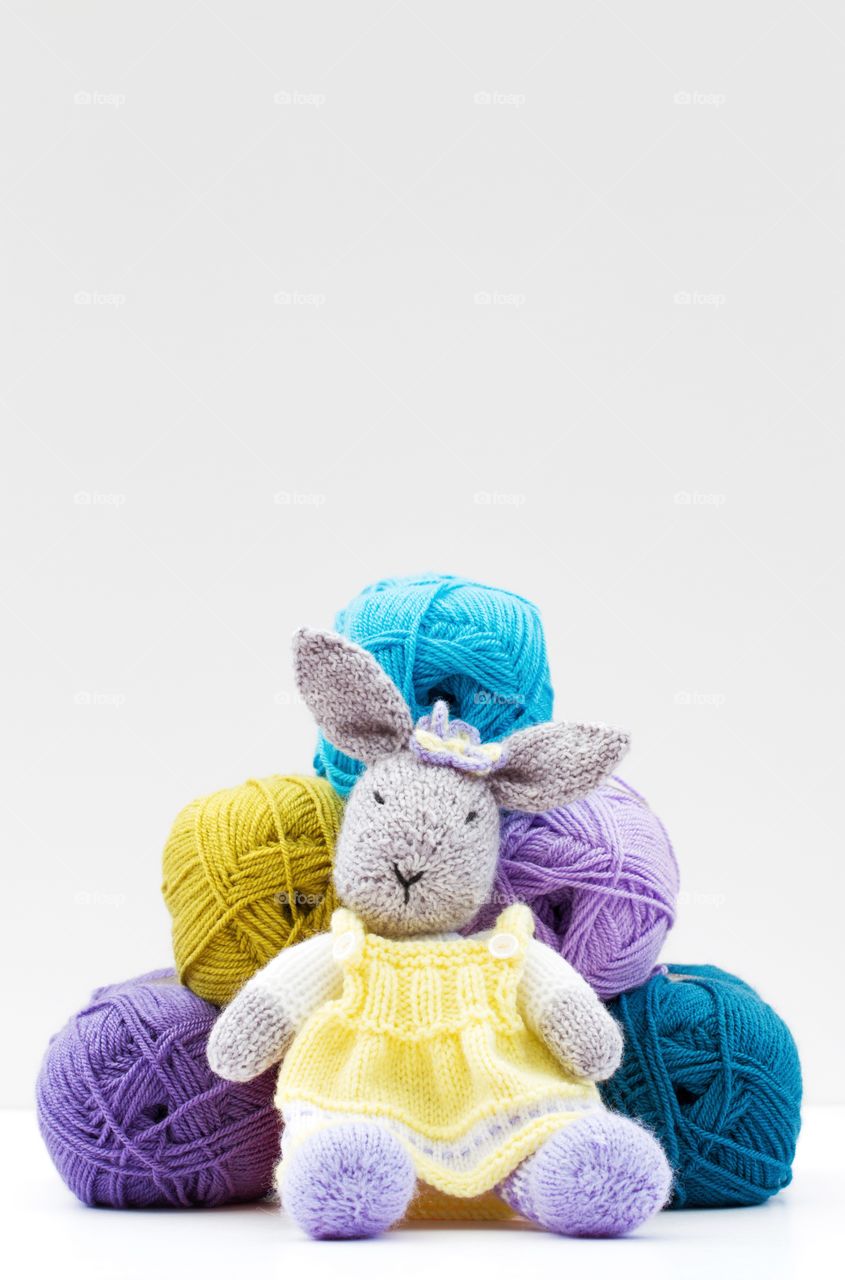 A woollen toy rabbit sitting in front of balls of wool.