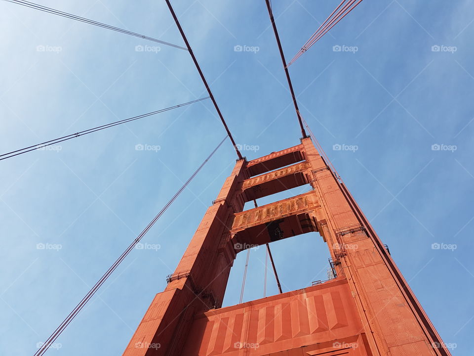 view looking up to red colored Golden Gate Bridge in San Francisco, America, on sunny blue sky day