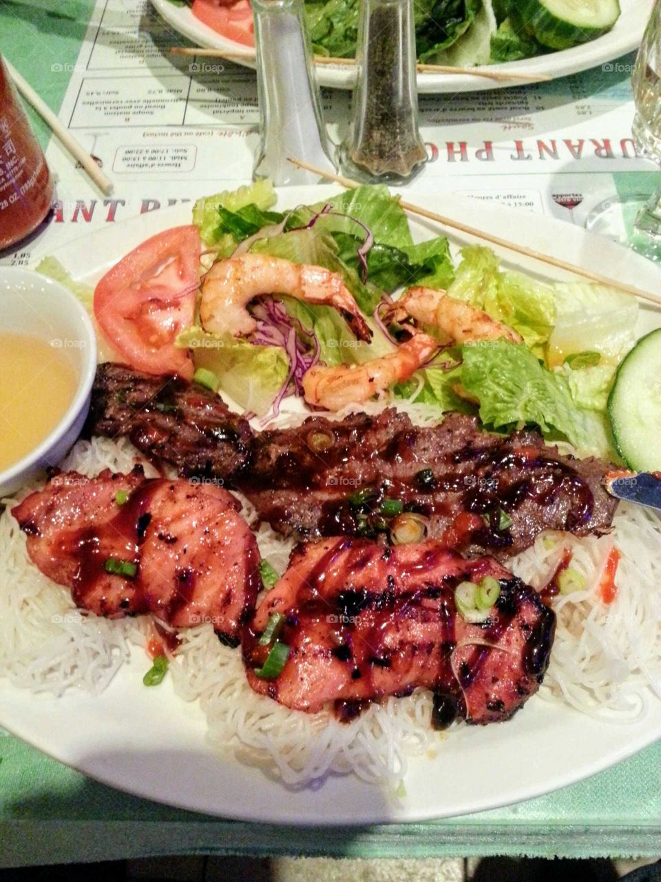 Chicken, beef,  shrimps on rice noodles with sauce and a green salad with tomatoes