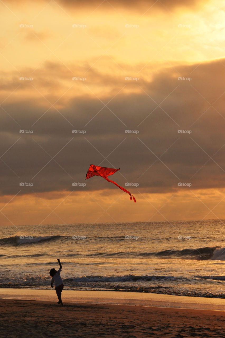 Kid playing with a kite on the beach at sunset 