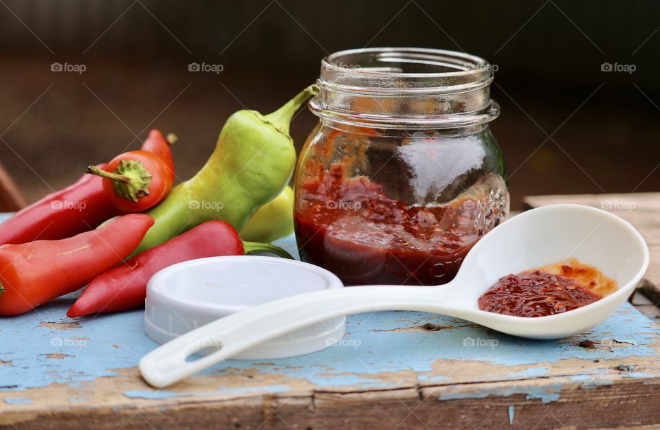 Canning peppers, chopped pepper preserves in jar and on ladle, atop weathered rustic wood outdoors