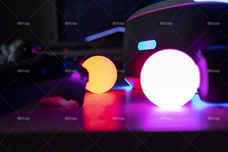 A portrait of a ps4 controller, and ps4 move controllers with light emitting globes on them and a ps vr headset. all turned on making a colorful scène with a lot of different lights.