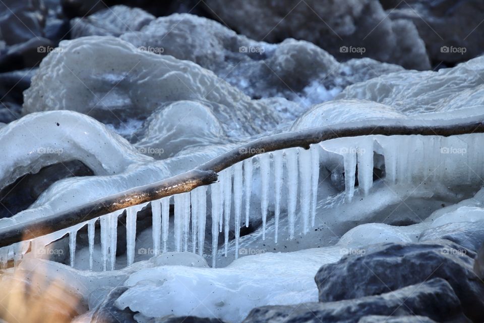 Icicles hang from stick and ice forms rocks laying near Lake Erie Ohio