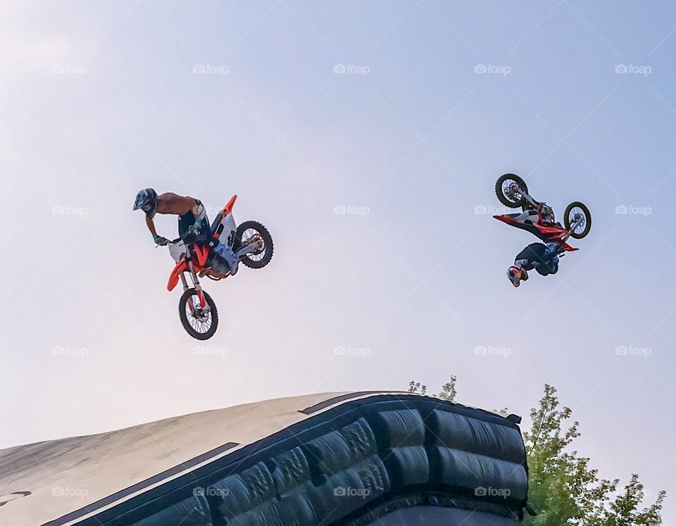 Motocross riders fly upside down and into the sky over a ramp 