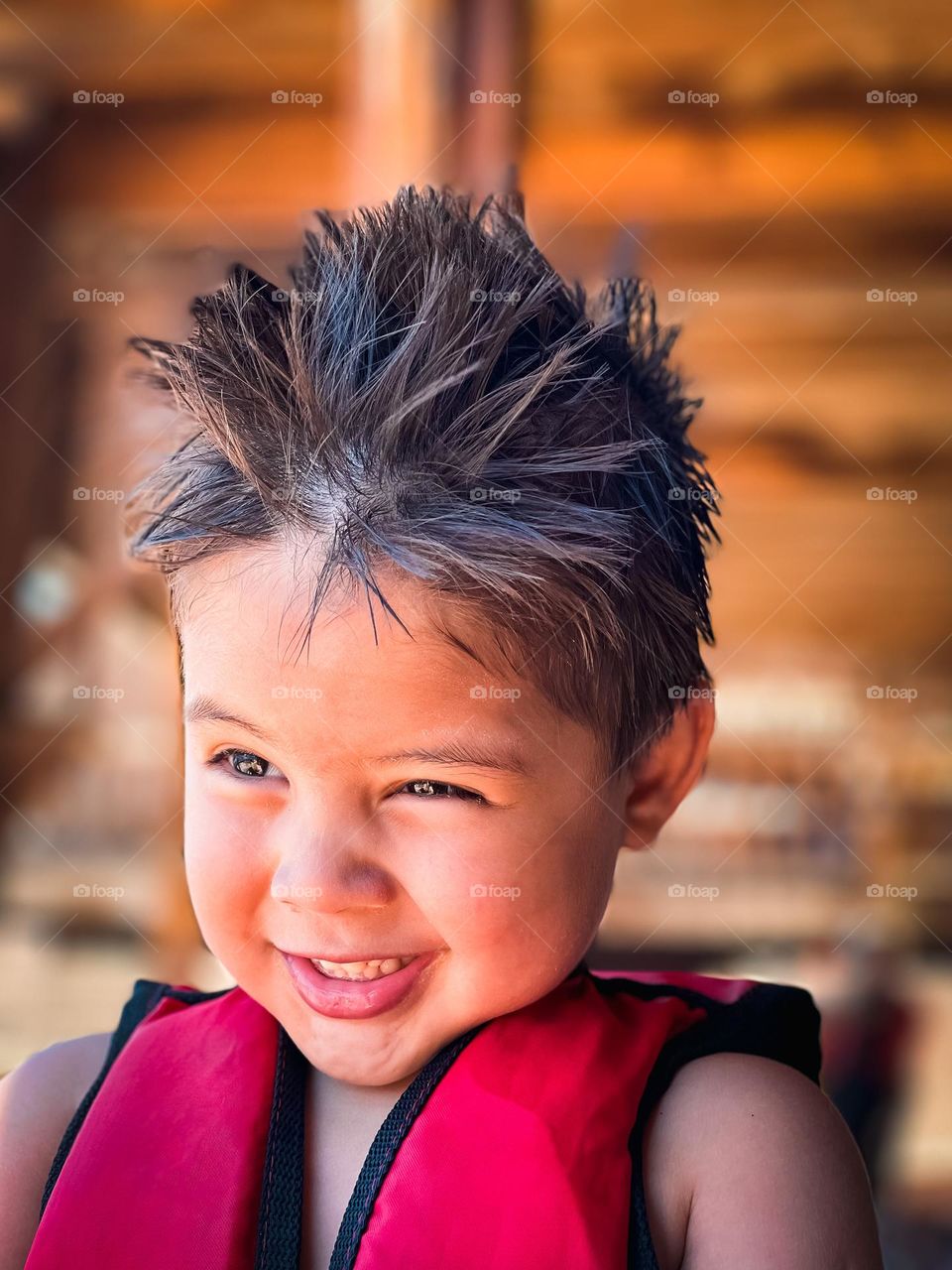 A 3 year old boy, wearing a life jacket in a sunny ambience.