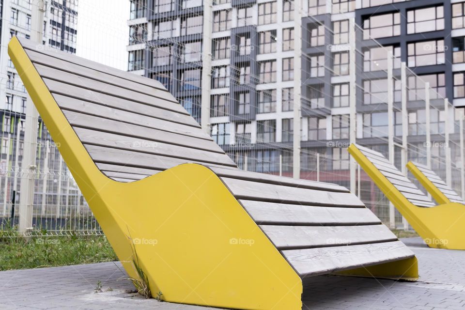 Modern, wooden bench with yellow edges in a metropolis. Corner of silence and calm.