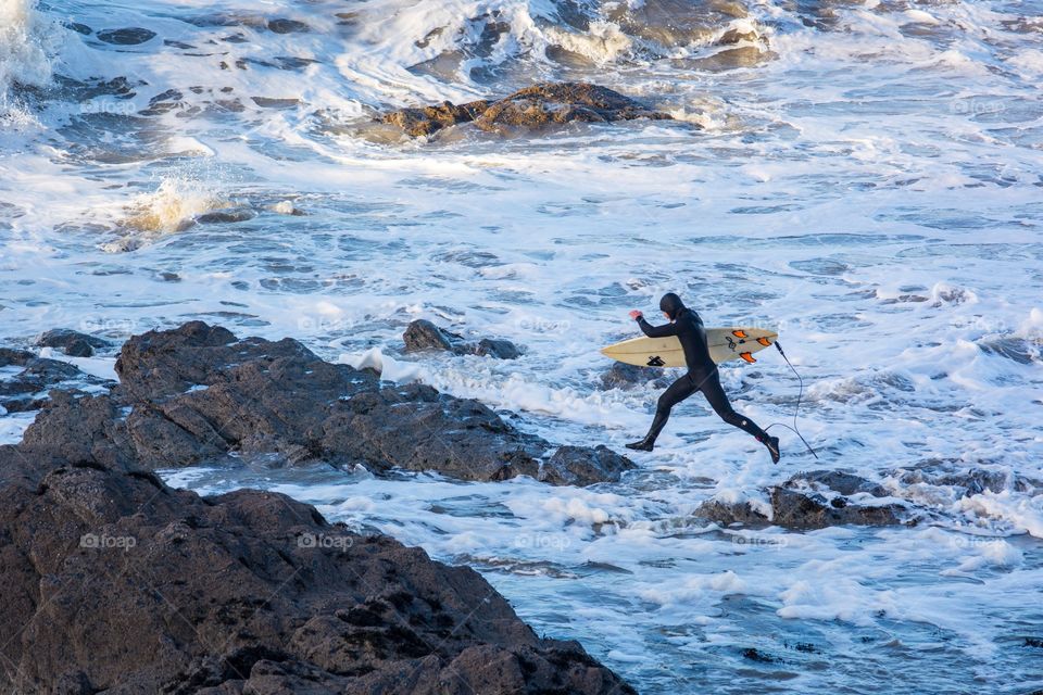 A surfer upping from rock to rock in search of the best wave. 