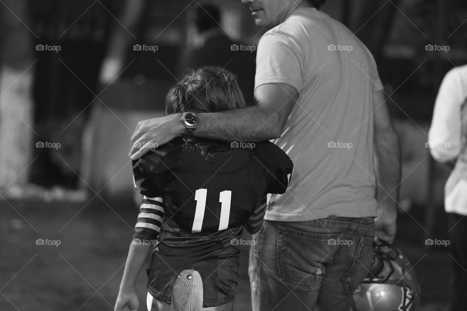 Young football player kid and dad. Dad hugs his little son after a football match