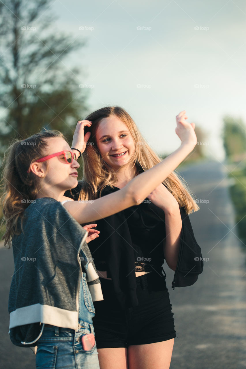 Teenage smiling happy girls having fun walking outdoors, hanging, spending time together on summer day. Real people, authentic situations