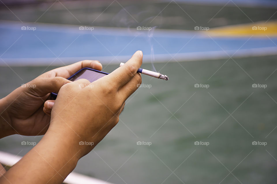 Hand holding a cigarette and a telephone. Background on basketball court