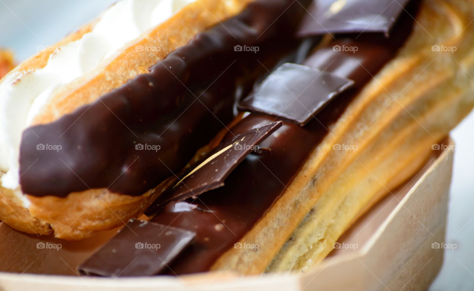 Chocolate squares in pieces with gold food paint on rich chocolate covered eclair with whipped cream filling French pastry decadent gourmet dessert photography  