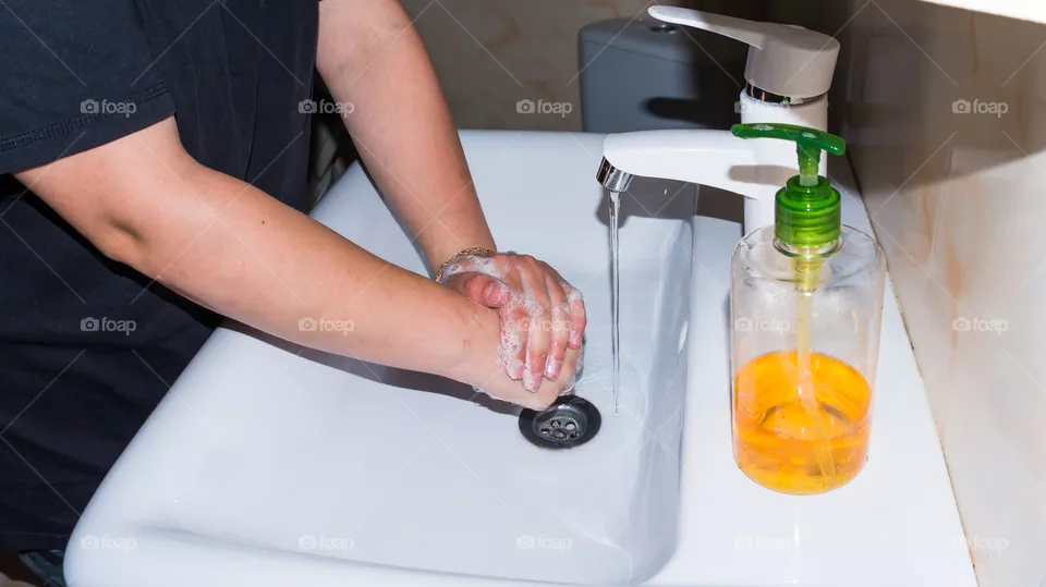 A man thoroughly washes his hands with soap in the bathroom, in a white washbasin with a white tap and antibacterial soap, makes a lot of foam and washes fingers and brushes after walking on the stree