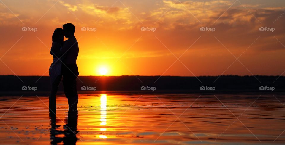 Silhouette of couple kissing in sea at sunset
