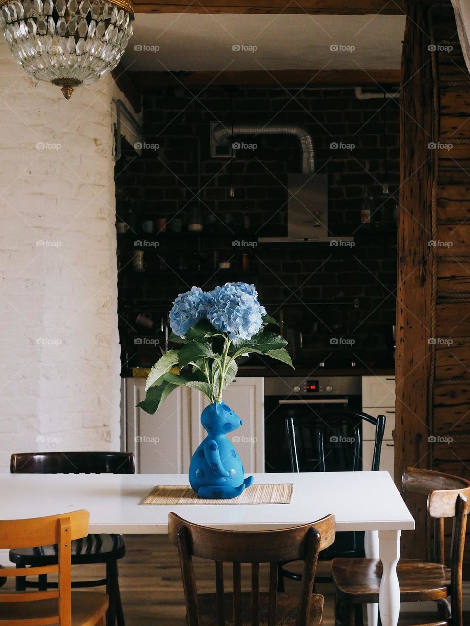 Bouquet of blue hydrangeas in general in the shape of a bear stands on a wooden table in a cozy kitchen