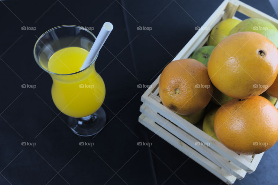 Oranges and glass tumbler with orange juice on black background