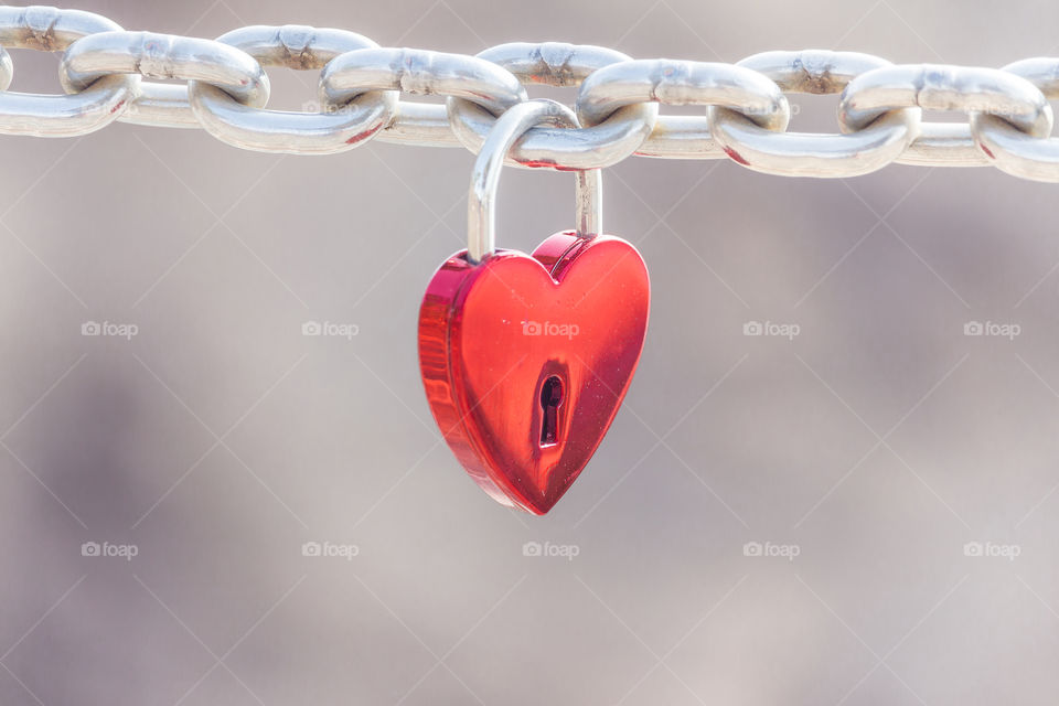 Red hart shaped padlock hanging from a steel chain