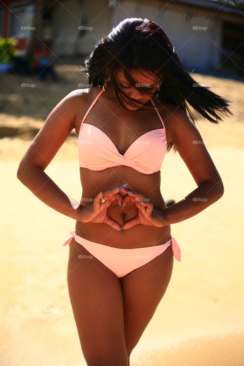 girl on the beach, with her hands on stomach in shape of a heart. latina with her hands showing heart