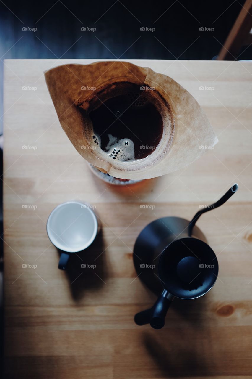 Chemex coffee about to be served into a ceramic mug on a table with some soft light. 