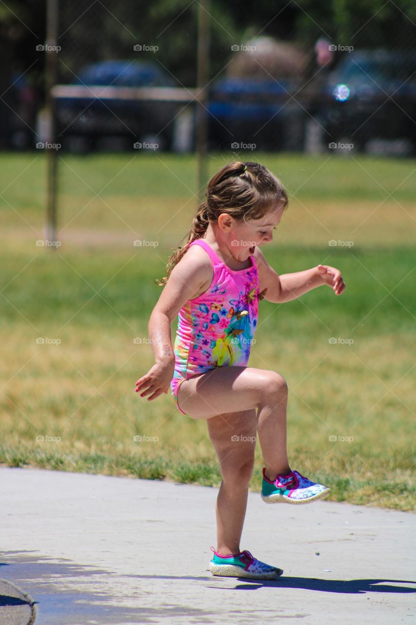 3 year old toddler celebrating on her birthday at the splash pad at the local park on a hot summer day 