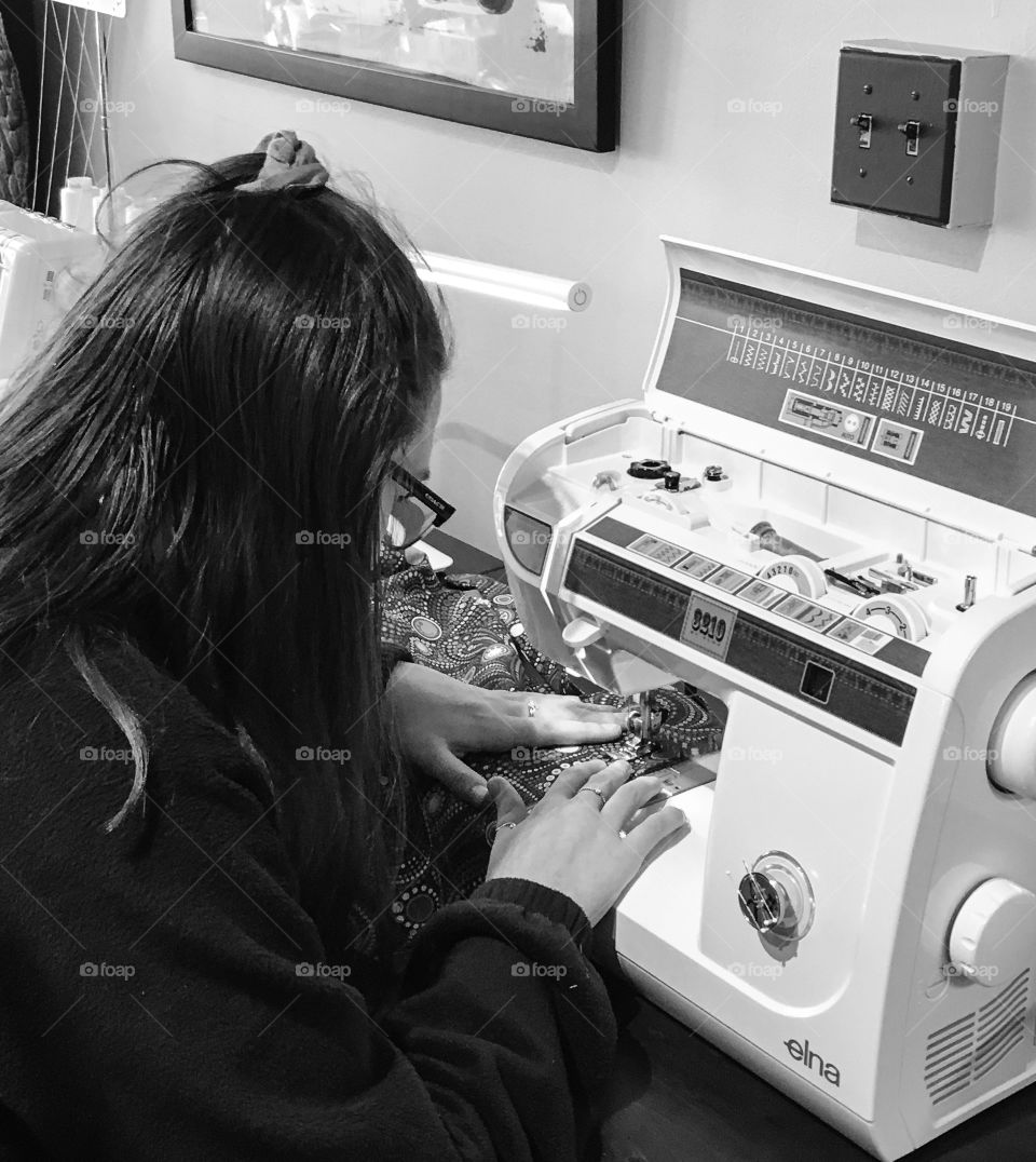 Teenage girl learning to sew on a machine.  She is concentrating on her stitching. 