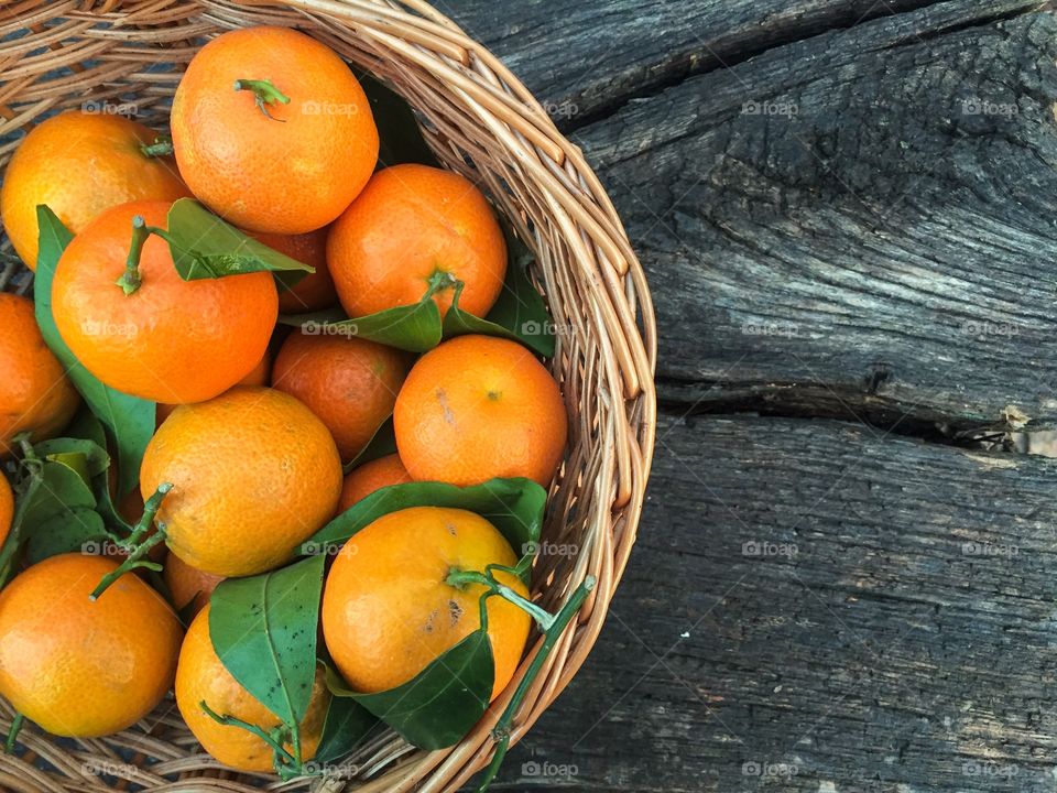 Wooden basket filled with mandarines and mandarine leaves on wooden table 