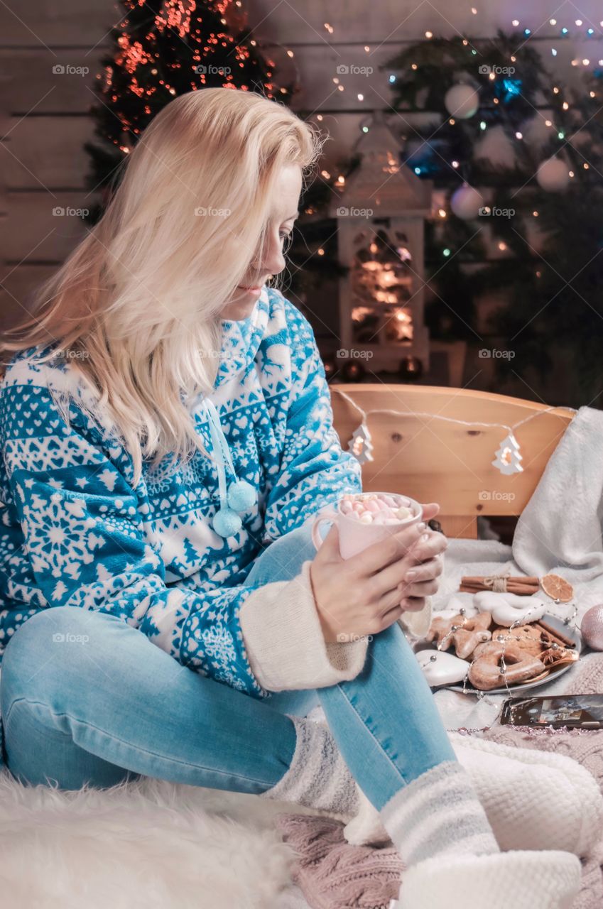 Cup with marshmallows in female hands on a background of Christmas decor