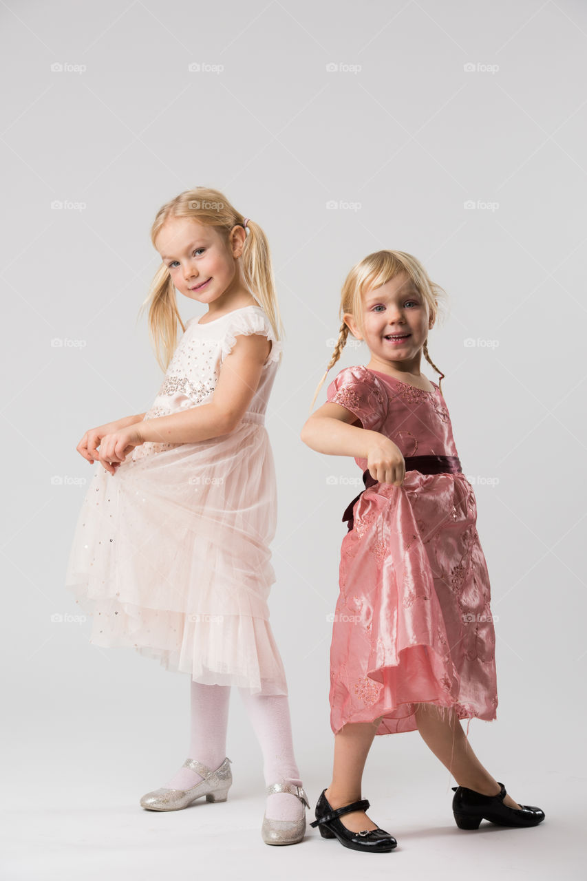 Two young sisters is posing with their beautiful dresses.
