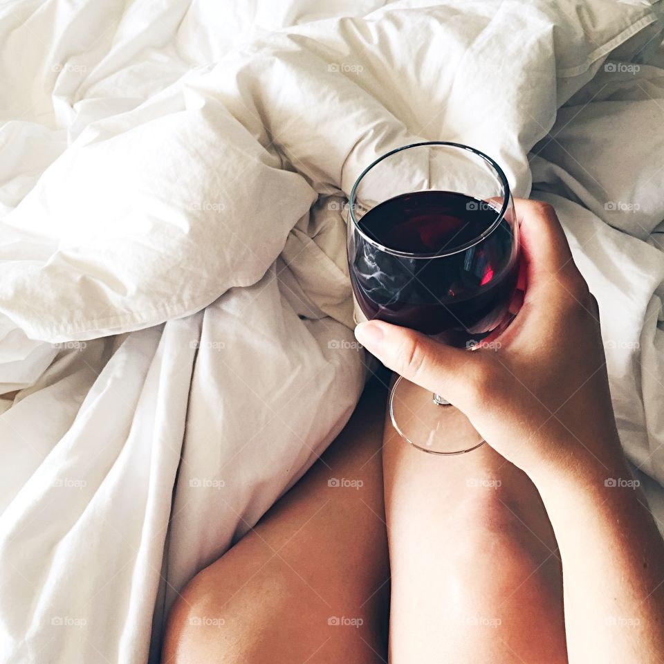 Close-up of woman holding wine glass on messy bed