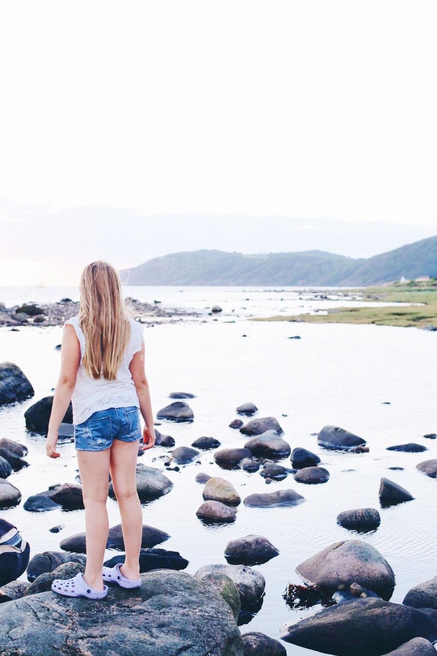 Girl with long blonde hair standing by the ocean in summertime 