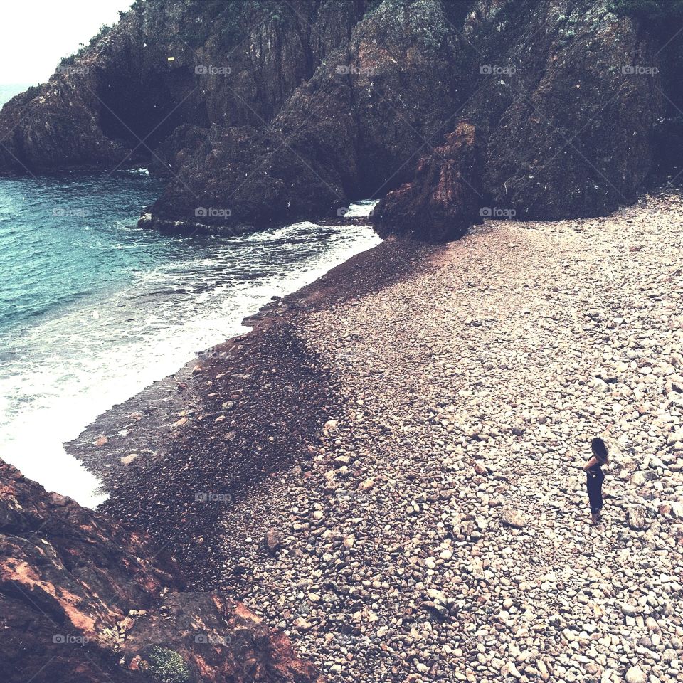 Girl alone on rocky Mediterranean beach. Girl alone on rocky Mediterranean beach with blue water and cliffs surrounding. 