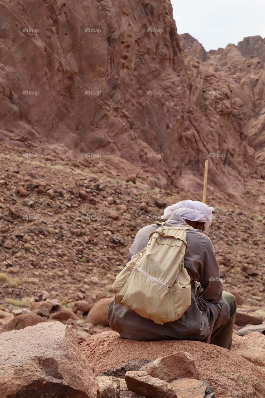 An old Bedouin man sit on a rock at the mountains taking a break 