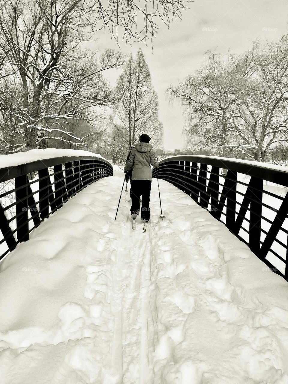 Cross country skiing across a snow covered bridge.