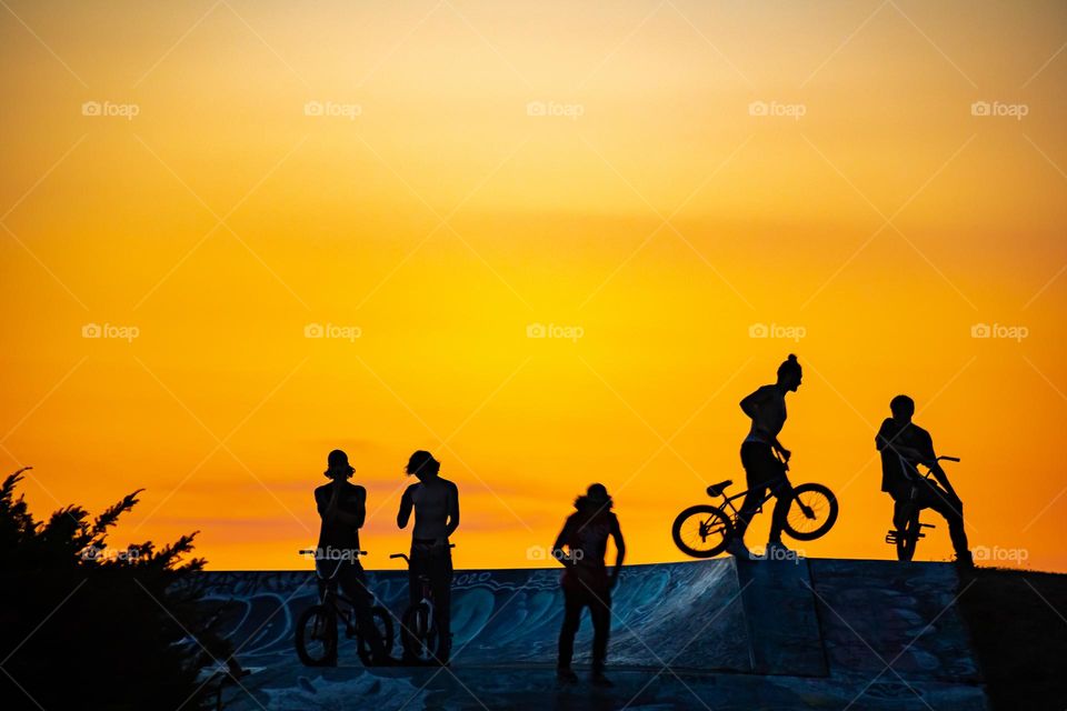 Silhouettes of Athletes riding BMX bikes at a skate park during sunset 
