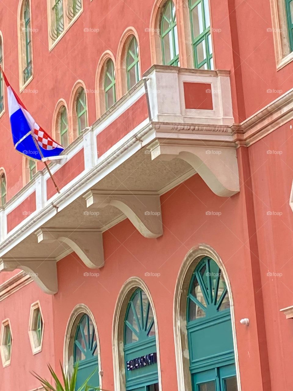A salmon pink building with teal arched doors and windows.