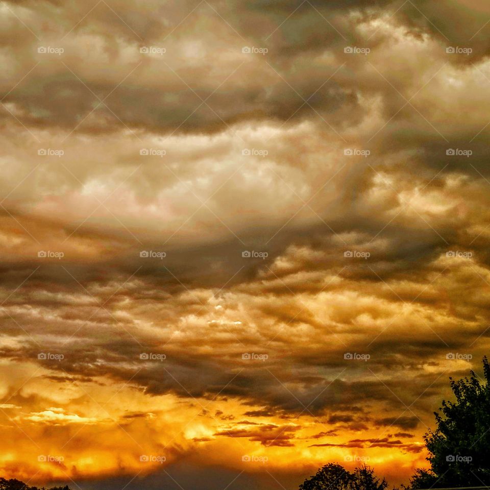burning orange sun setting on the horizon beneath a blanket of ominous storm clouds.