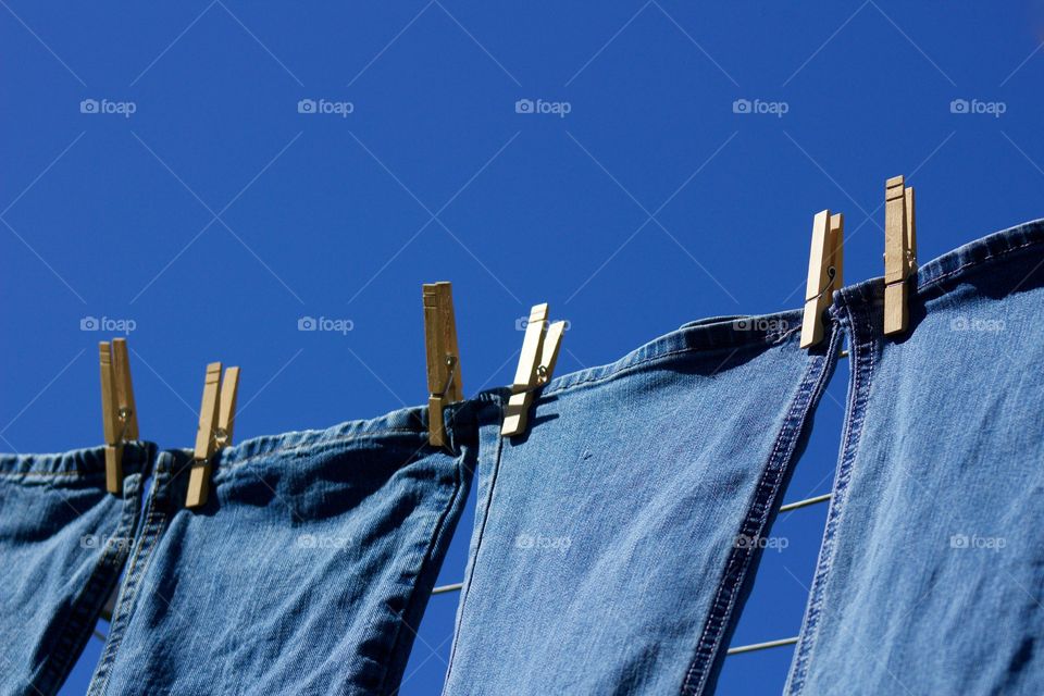 Freshly laundered blue jeans hanging on a clothesline in the sunshine against a blue sky