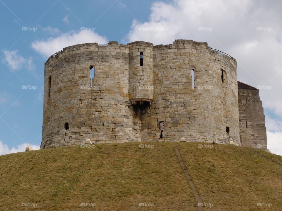 Clifford’s Tower, a local stone landmark in York in England, sits majestically on top of a hill on a sunny day. 