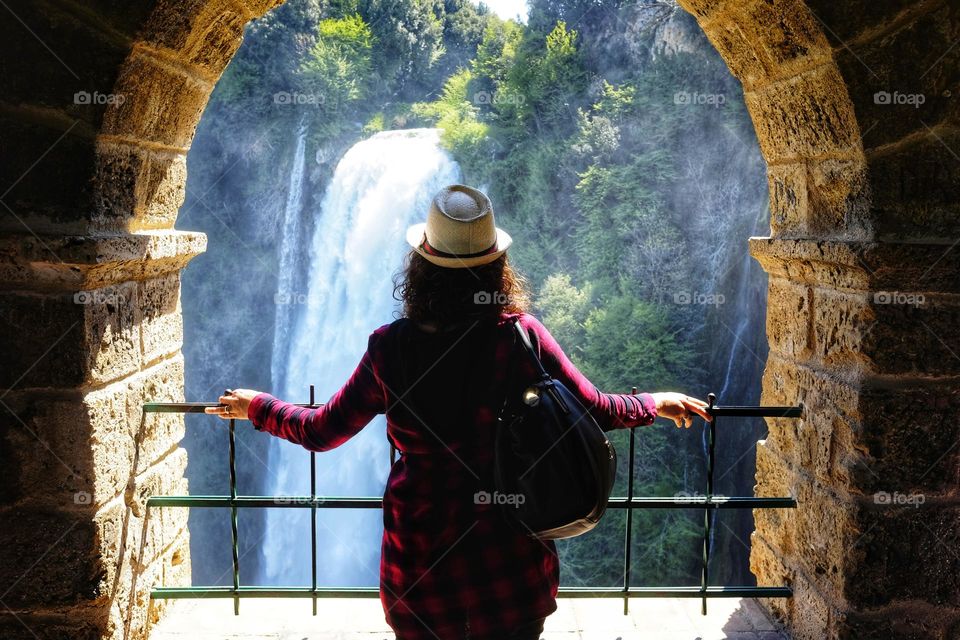 woman from behind with hat looks out of the window at the Marmore waterfall in Umbria, Italy