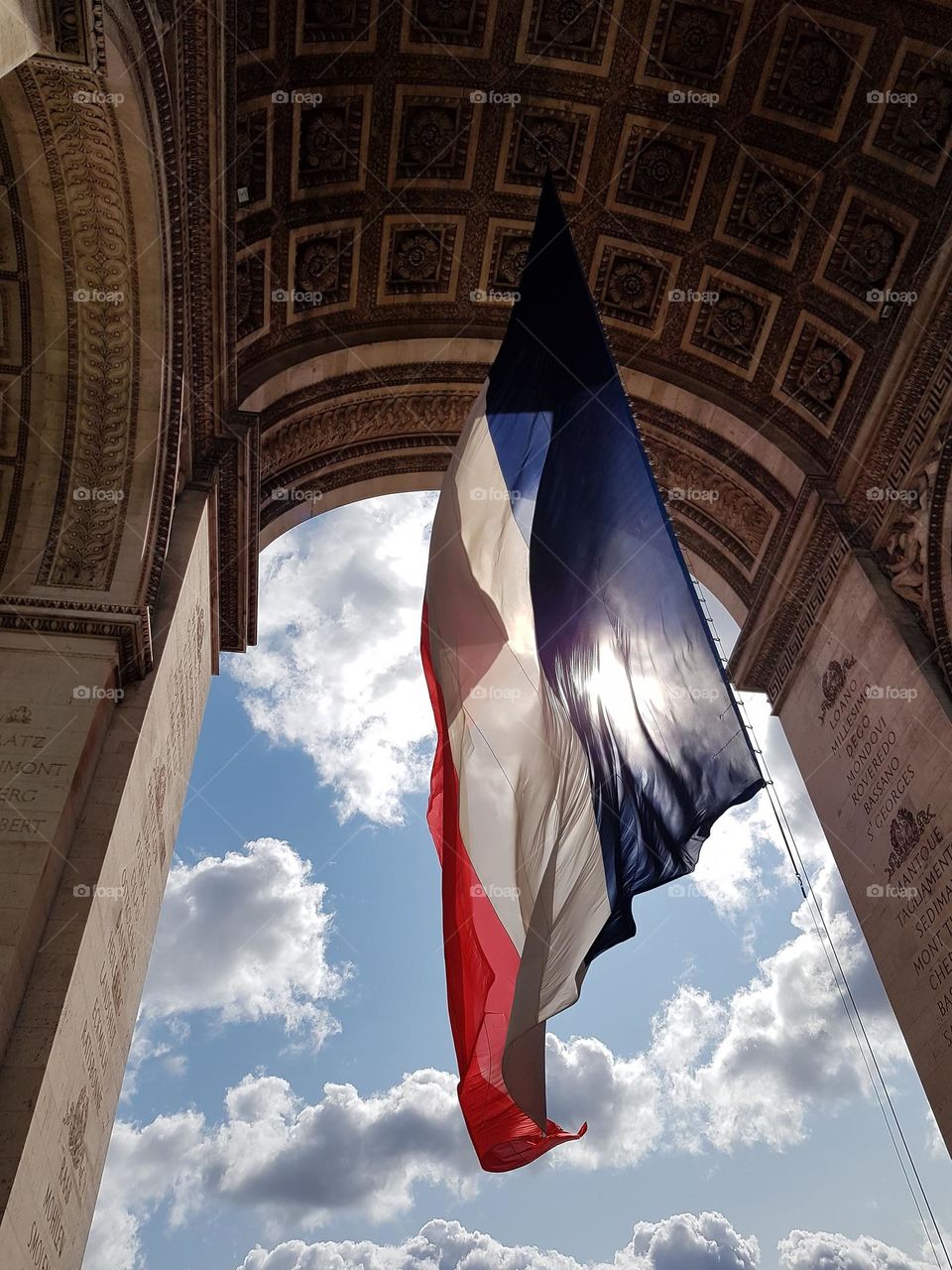 View of the French flag and a cloudy blue sky underneath the Arc de Triomphe in Paris