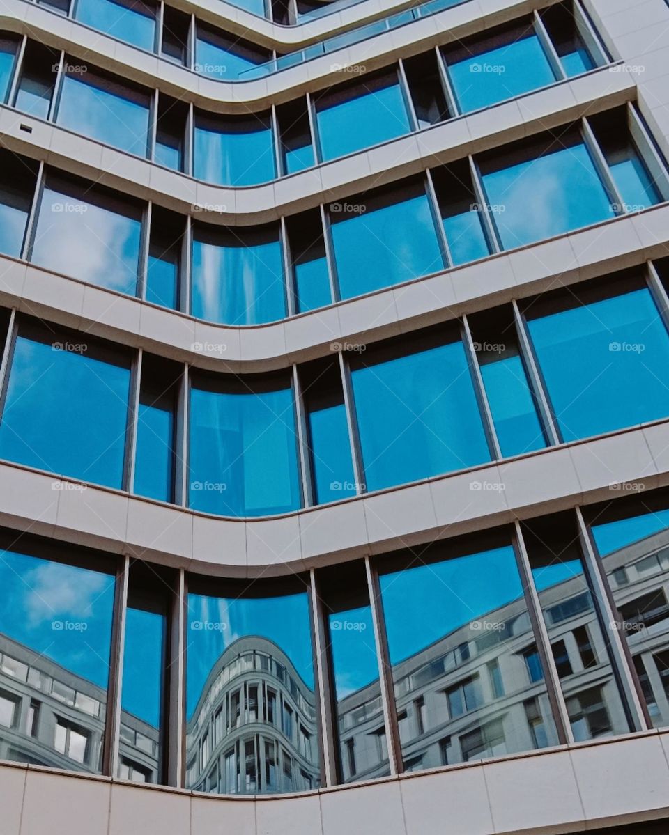 Glazed front of a building with reflection of a blue sky and of an other building