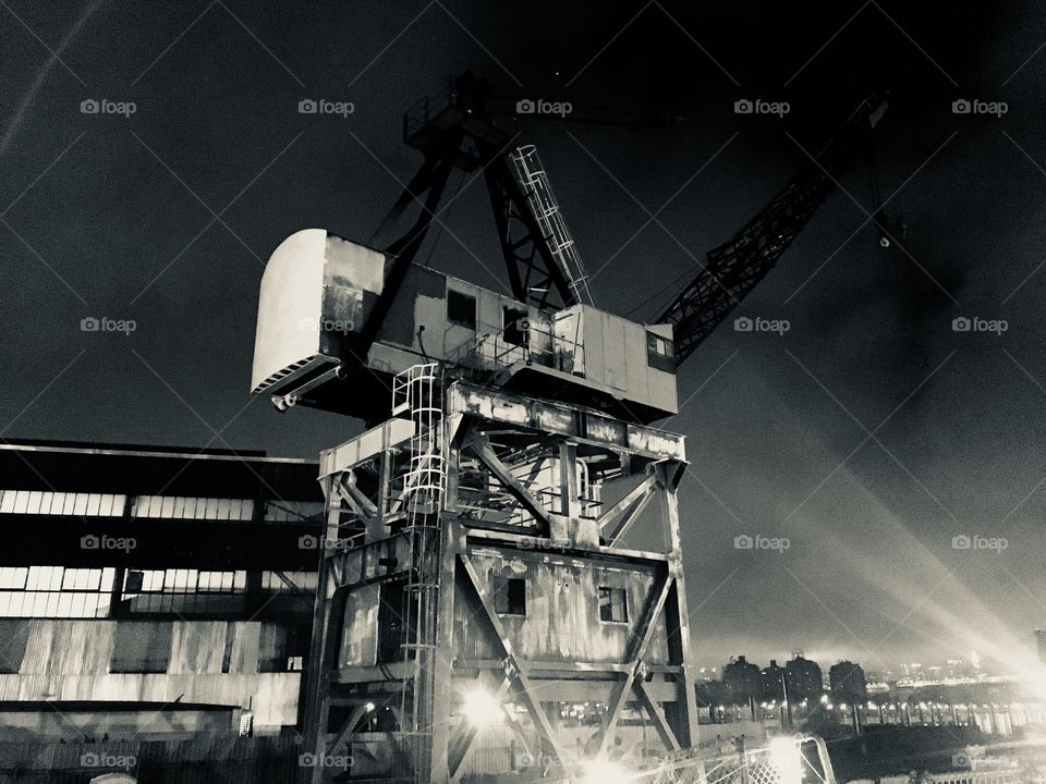 Night time view of crane, shipyard operations, New York pier. 